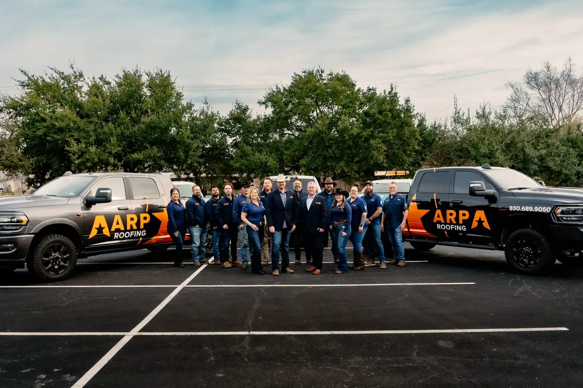 ARP Roofing team of 20+ employees standing between two branded service trucks in parking lot