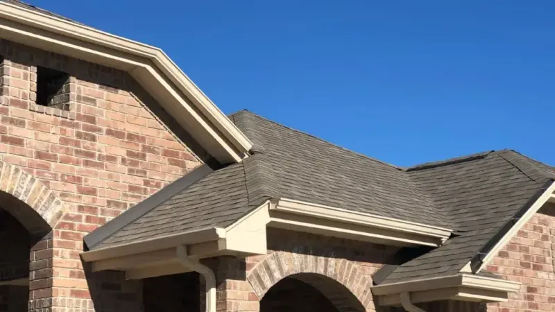 Architectural asphalt shingle roof on brick residential home with arched entryway and gable vents under clear sky