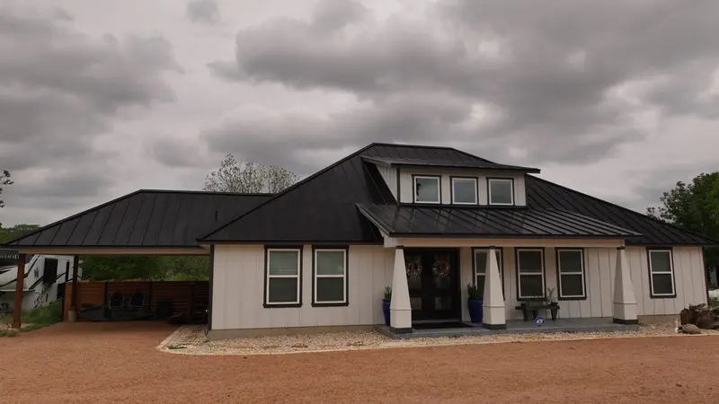 Modern residential home with black metal standing-seam roof, white exterior, multiple gables, and dormer windows