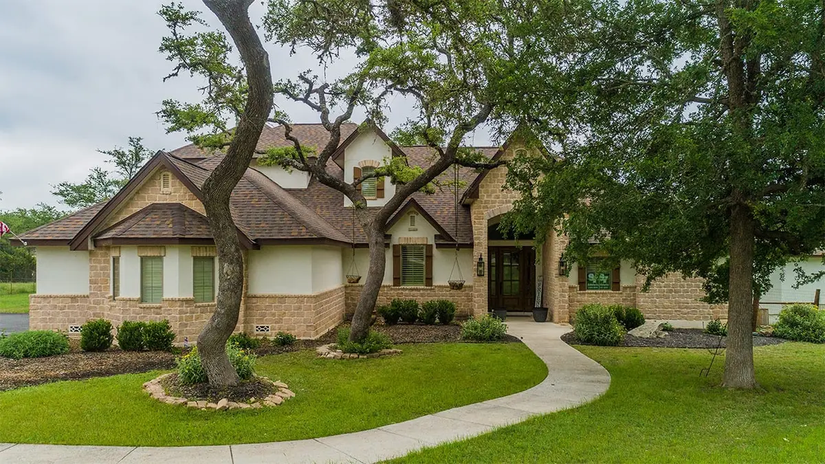 Brick residential home with architectural shingle roof, multiple gables, and mature oak trees in landscaped yard