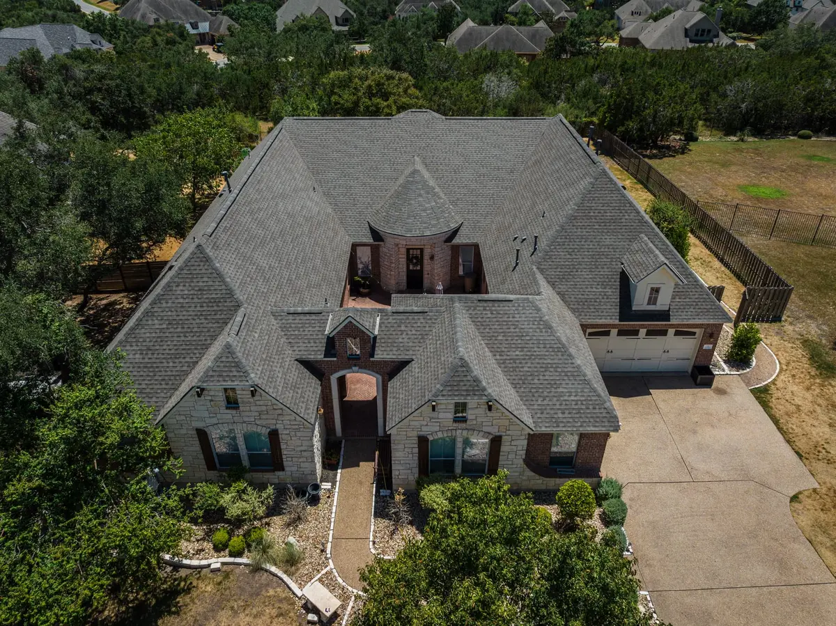 Aerial view of two-story brick home with gray architectural shingle roof, brick turret, and attached garage in residential