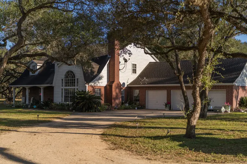 Two-story brick house with white siding addition, dark asphalt shingle roof, brick chimney, under mature oak trees