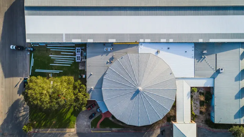 A large circular standing-seam metal roof on an industrial building — the ag and warehouse stock ARP details for wind, drainage, and decades of South Texas sun.