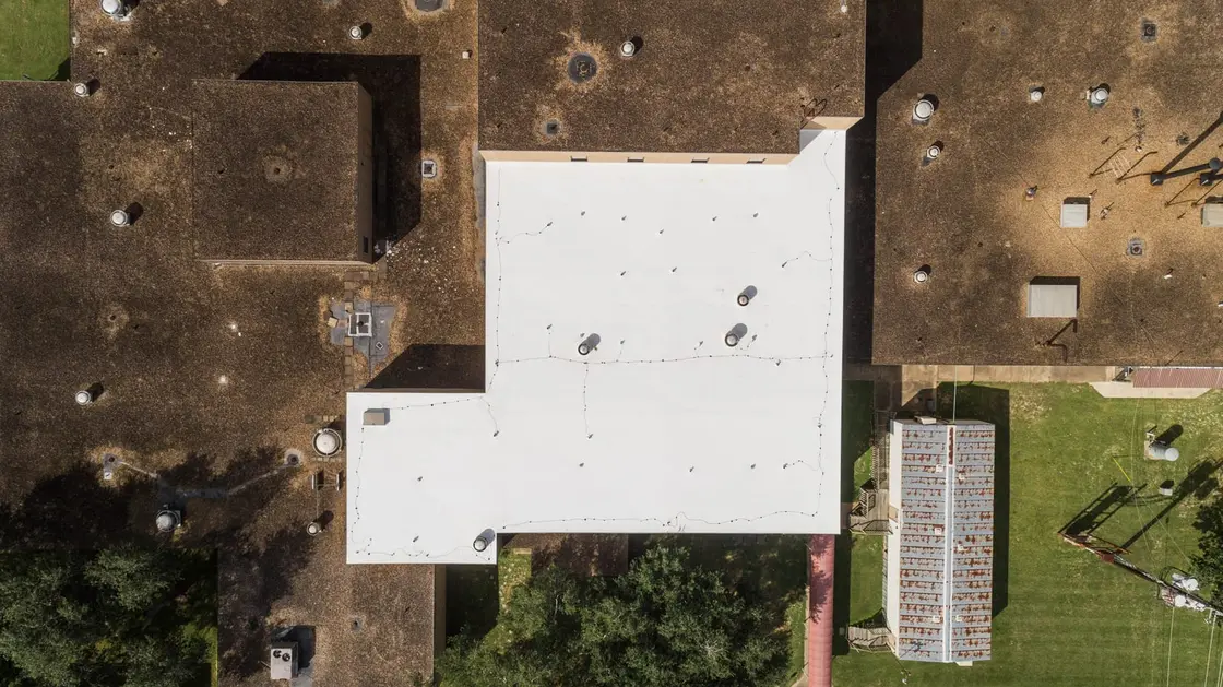 Overhead drone view of a white single-ply flat roof section next to older, weathered flat roofs