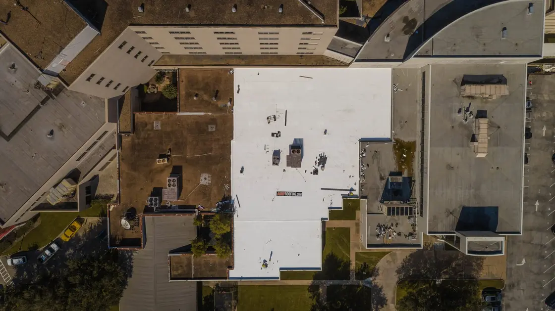 Overhead view of a white membrane flat roof section surrounded by older, darker flat roofs
