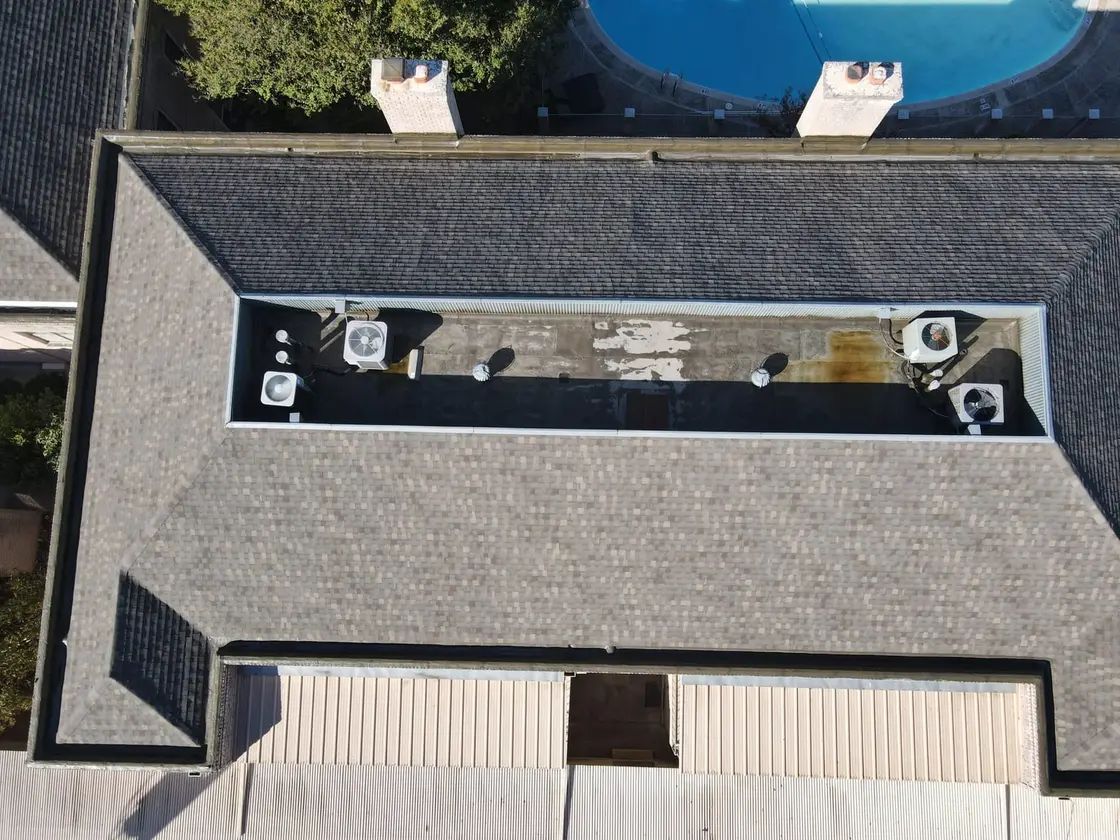 Drone view of an aging low-slope roof section with a stained, patched membrane and rooftop AC units, the kind of roof a moisture survey reads before any quote