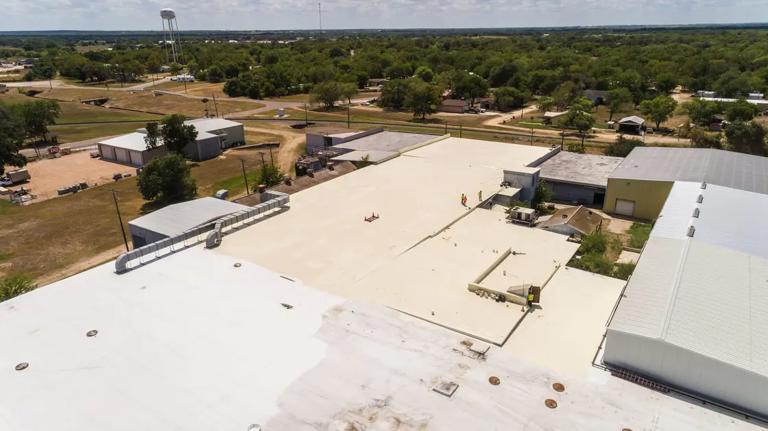Aerial view of a large low-slope commercial roof with a newly installed reflective single-ply membrane on a Texas building