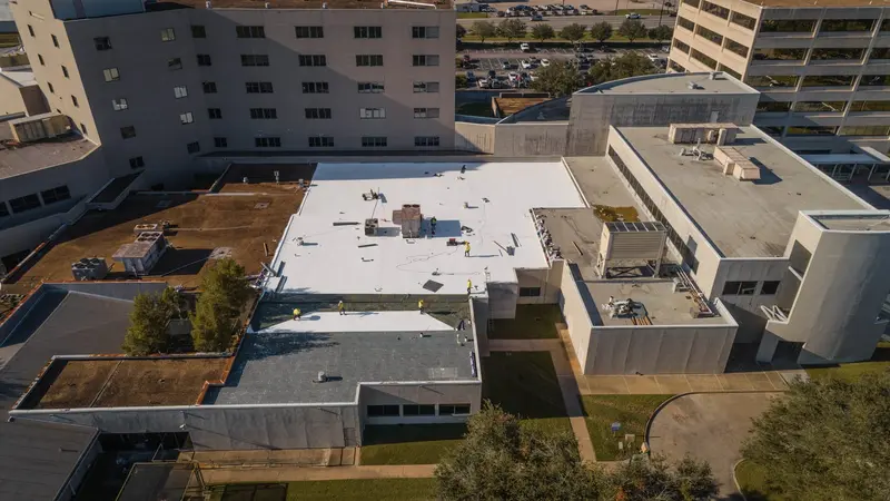 A crew working a white membrane roof section by section — on a repair, we trace the leak to its source before we quote the fix.
