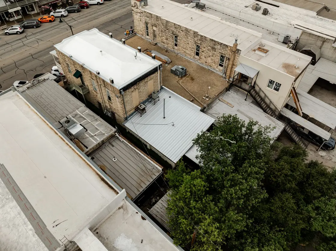 Low-slope roofs on neighboring buildings seen from above, where membrane seams and laps meet the parapet walls