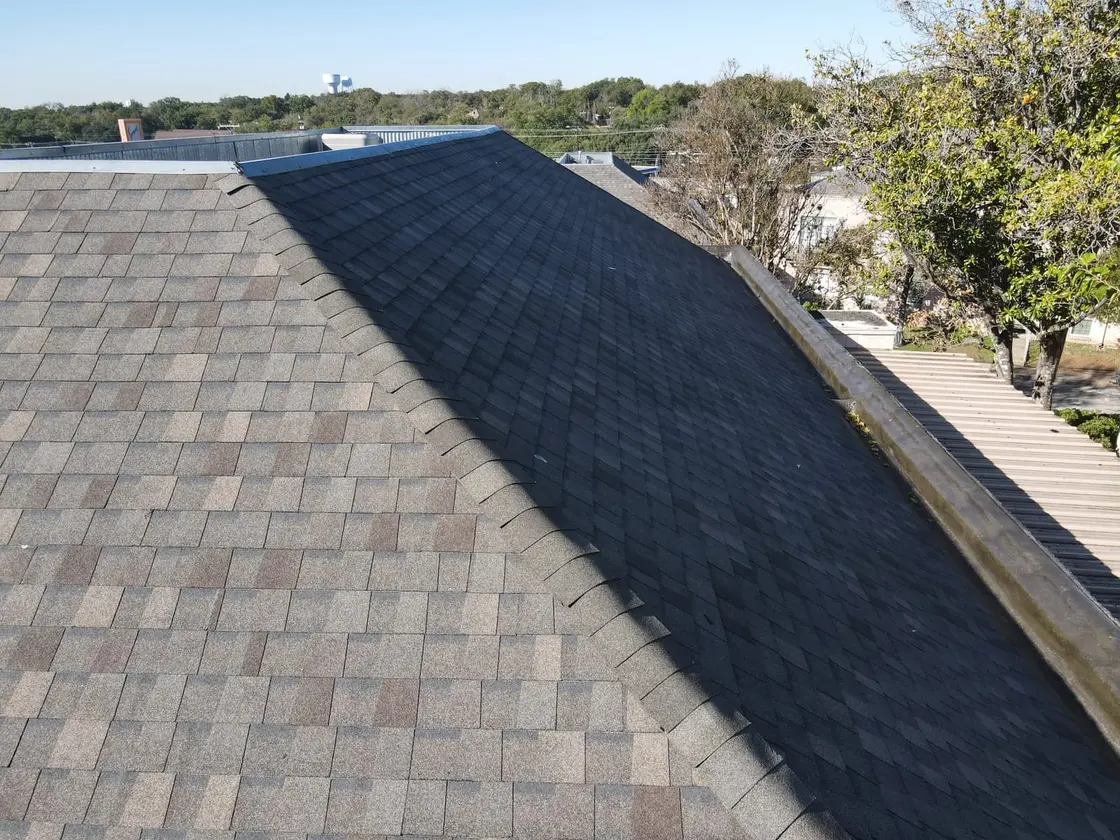 Metal gutter and downspout on a single-ply commercial roof edge in Texas where the drainage carries water to grade