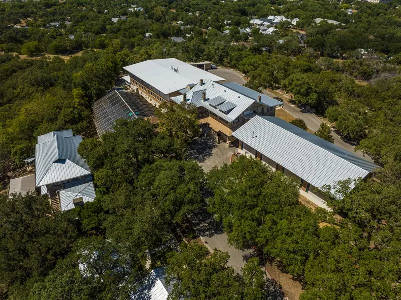 Aerial view of commercial buildings with white and gray metal standing-seam roofs surrounded by dense trees in rural setting.