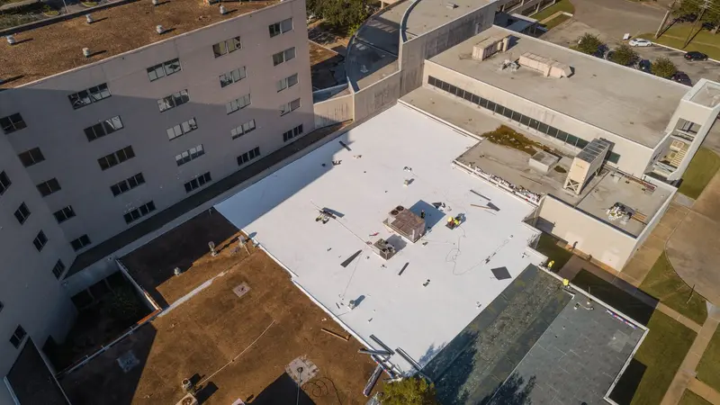 A white membrane roof among older low-slope sections — on a repair, we trace the leak to its source before we quote the fix.