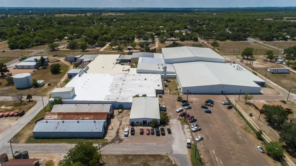 Aerial view of large commercial warehouse complex with white TPO flat roofs, parking lot with vehicles, blue storage tanks