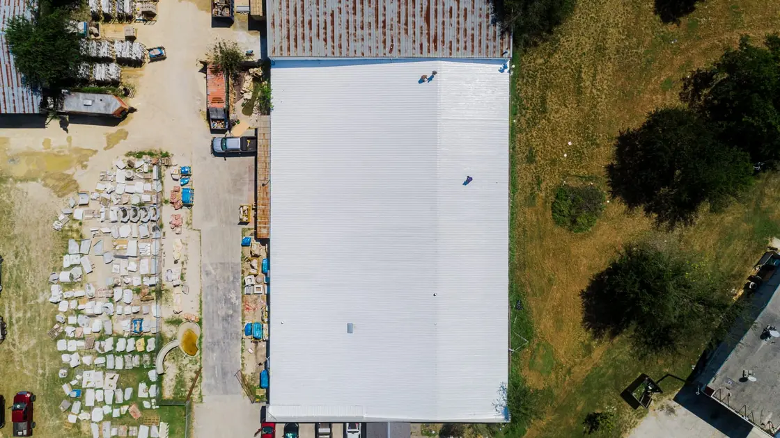 Two people walking a white low-slope commercial roof, seen from directly above