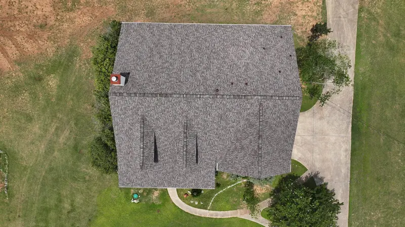 Aerial view of residential home with gray architectural asphalt shingle roof, multiple roof valleys, and concrete driveway.