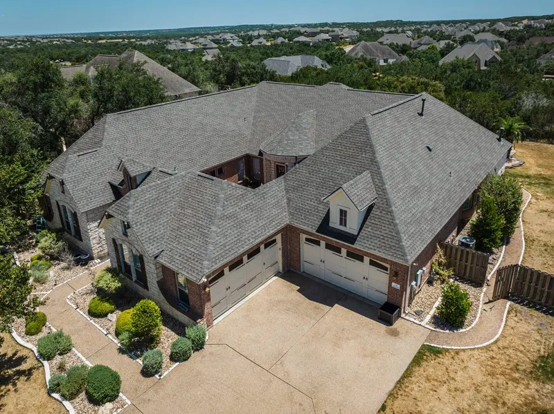 Aerial view of brick two-story home with gray architectural shingle roof, two-car garage, and manicured landscaping in