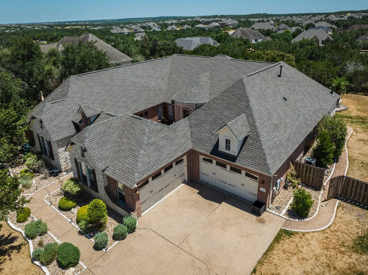 Aerial view of brick two-story home with gray architectural shingle roof, two-car garage, and manicured landscaping in