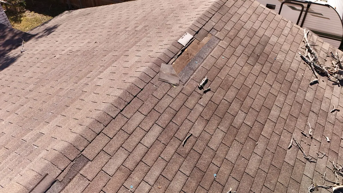 A brown asphalt shingle roof slope with shingles torn off and bare patches showing, in need of repair