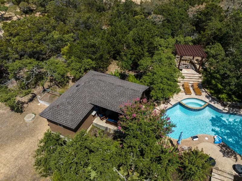 Aerial view of residential home with dark gray architectural shingle roof surrounded by native Texas Hill Country