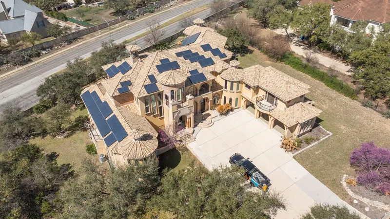 Luxury home with multiple roof peaks featuring dark solar panels on tan tile roofing, driveway with service vehicle