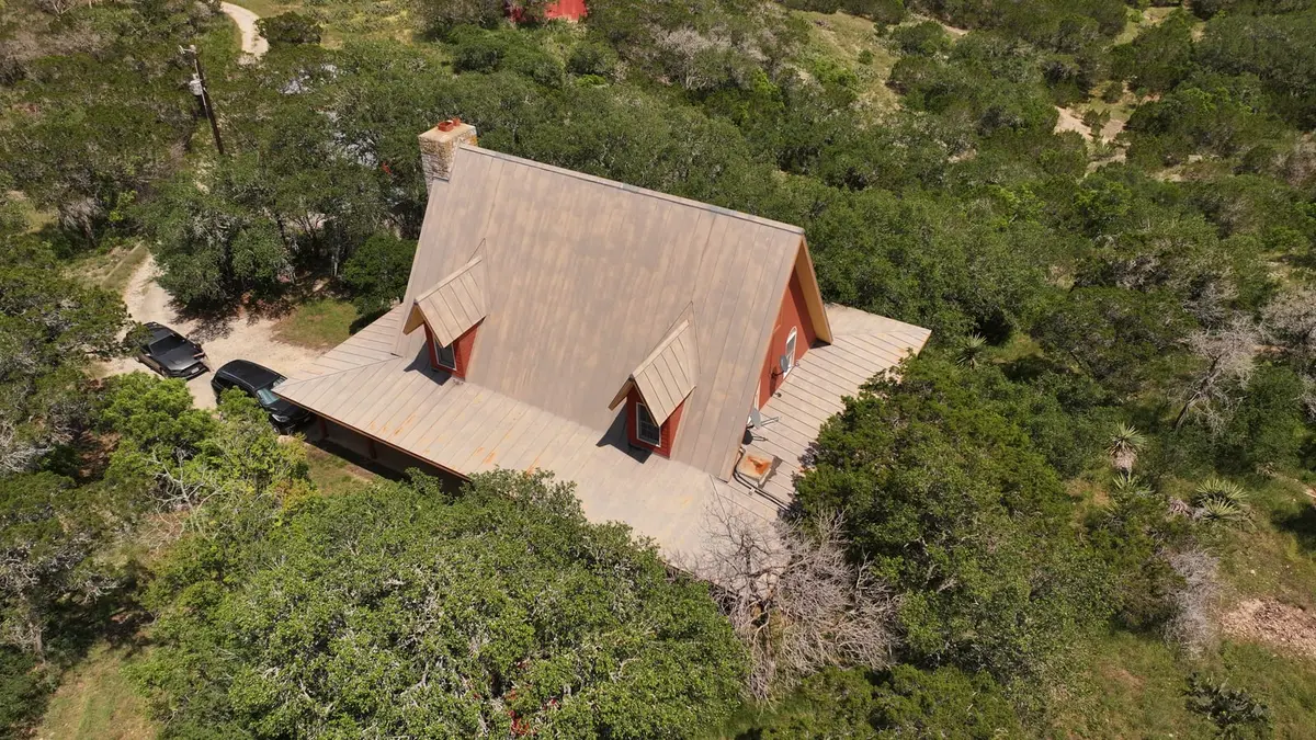 Aerial view of a-frame residential home with metal standing seam roof, red/rust siding, surrounded by Texas Hill Country