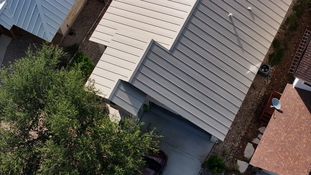 Aerial view of residential home with light gray metal standing seam roof and brick chimney
