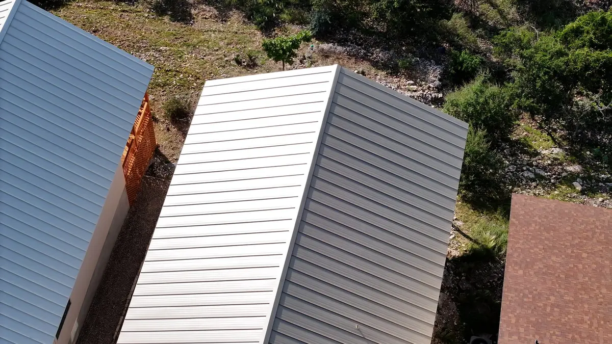 Multiple residential rooflines with metal and horizontal siding, hillside landscape with vegetation and stone.