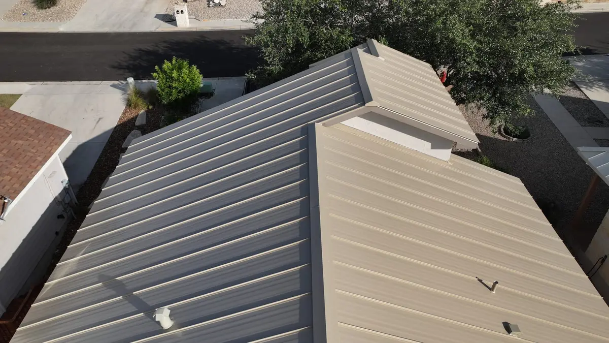 Aerial view of residential metal standing-seam roof in gray and tan colors with multiple roof planes and landscaping