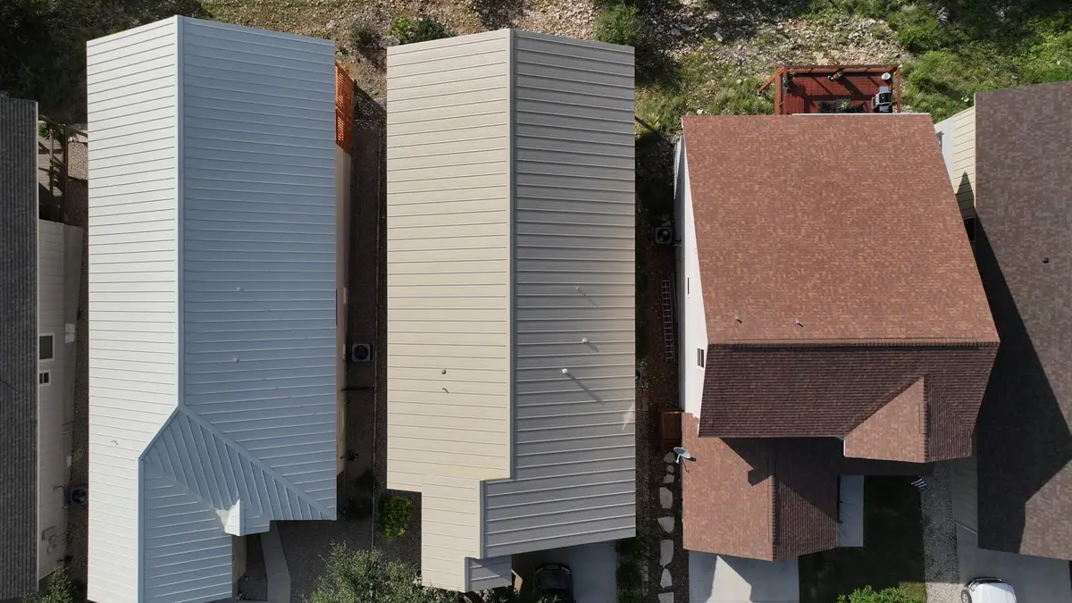 Aerial view of residential home with steep-slope metal standing-seam roof in gray and cream colors