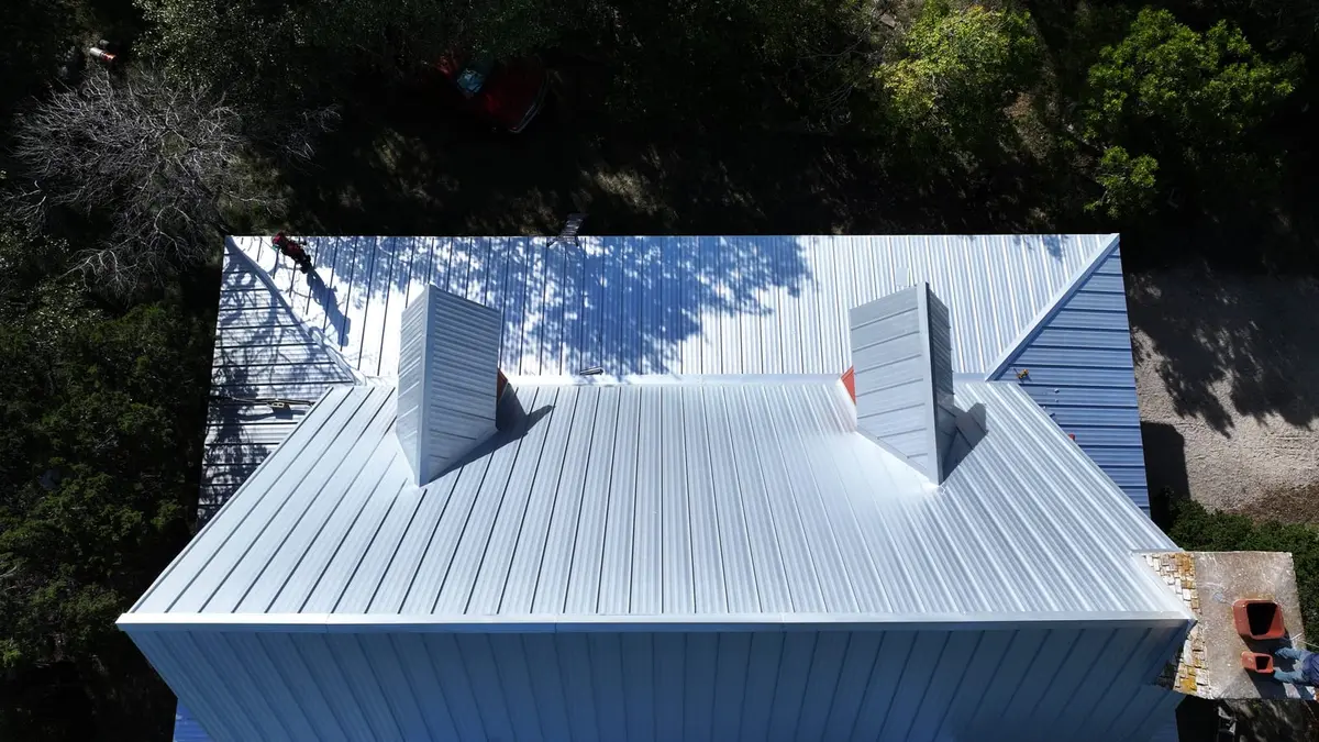Aerial view of residential metal standing-seam roof with two roof penetrations and surrounding trees
