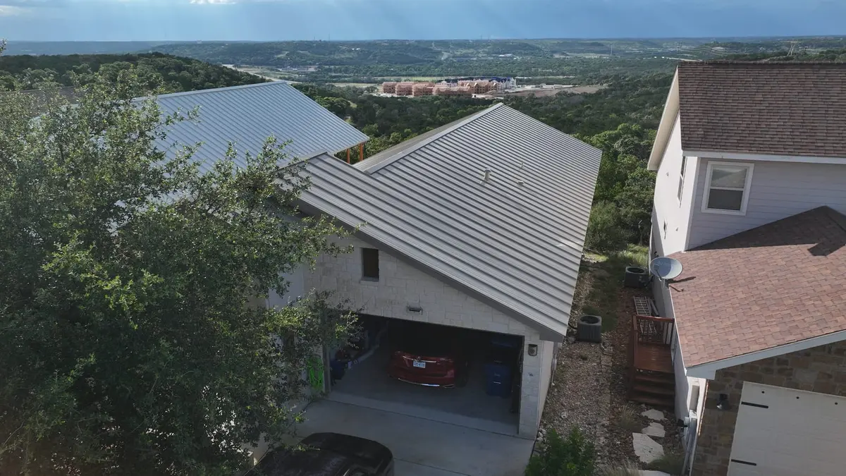 Modern home with gray metal standing-seam roof and white exterior, hillside location overlooking valley with residential