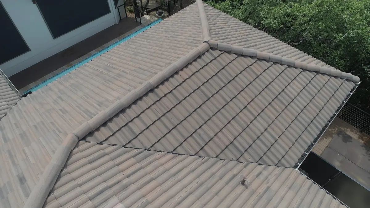 Aerial view of residential roof with metal standing seam panels installed on steep slope, showing ridge cap and adjoining