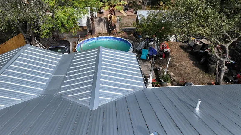 Metal standing-seam roof installation on residential home with pool visible in backyard