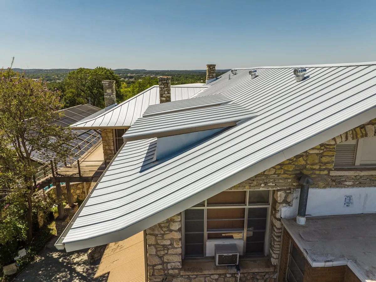 Metal standing seam roof with multiple chimneys and stone exterior on hillside property overlooking valley landscape.