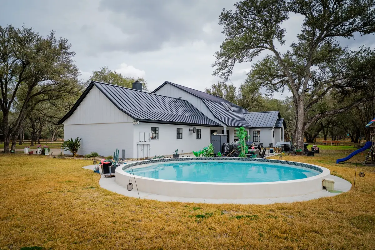 White farmhouse with a black standing seam metal roof beside a round in-ground pool