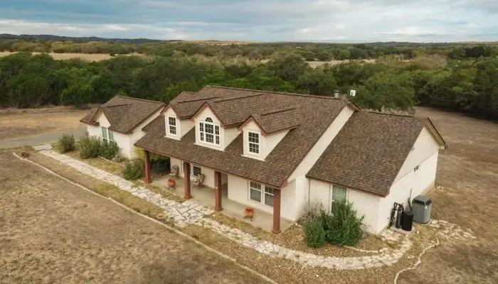 Aerial view of a Texas Hill Country ranch home with a brown architectural shingle roof