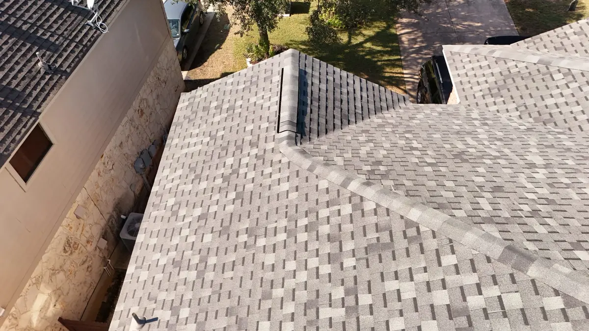 Aerial view of new architectural asphalt shingle roof installation on residential home with light gray shingles and metal