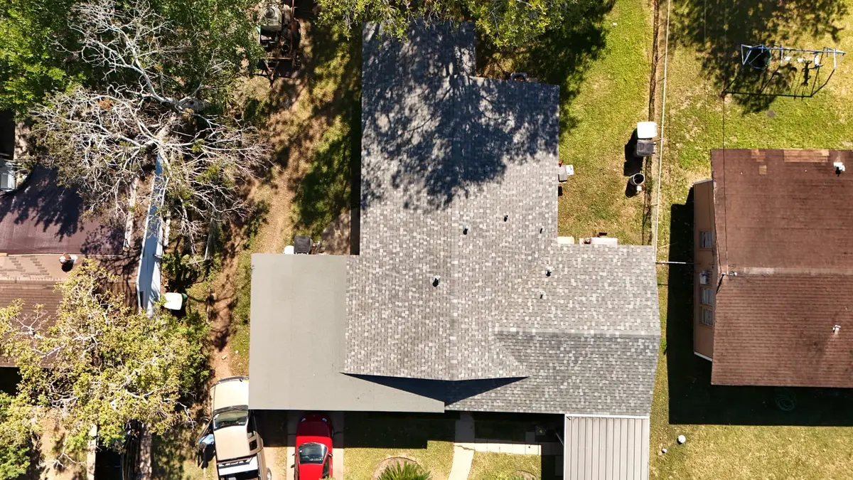 Aerial view of residential home with new gray asphalt shingle roof installation, surrounded by green lawn and brick
