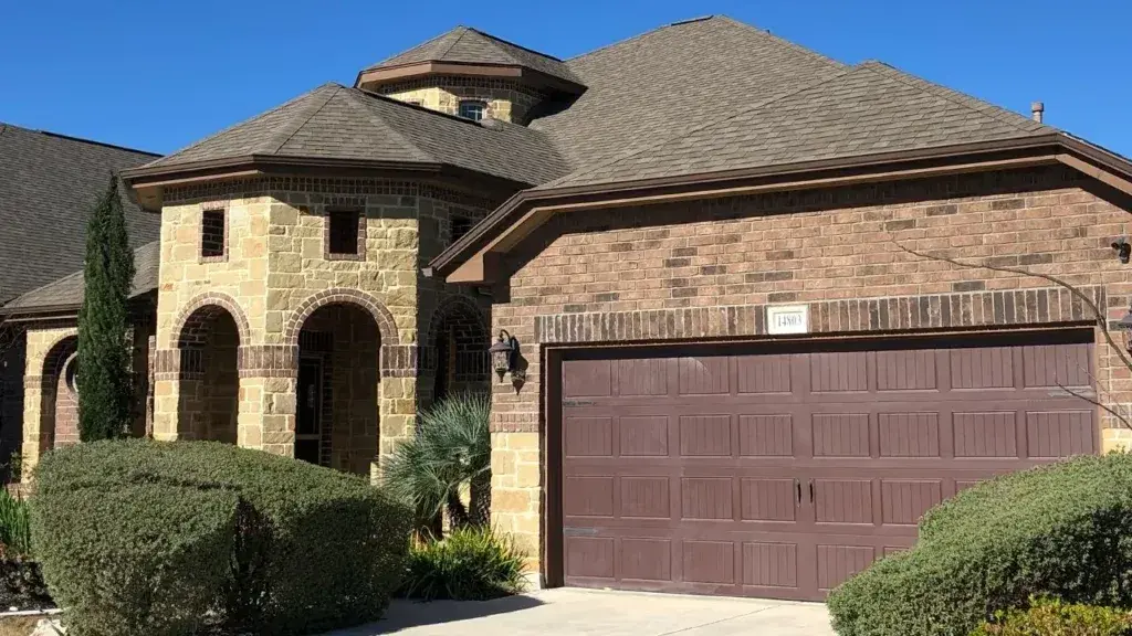 Two-story brick home with architectural asphalt shingle roof, multiple peaks, arched entryway, and brown garage door