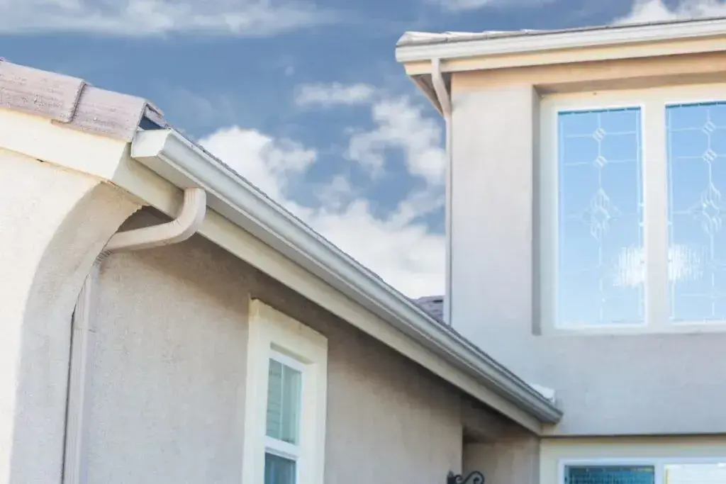 Seamless aluminum gutters and a downspout running down a white Texas home