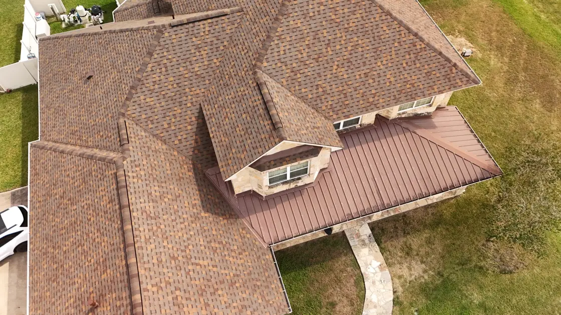 Residential home with brown asphalt shingles on the main roof and a metal standing seam section
