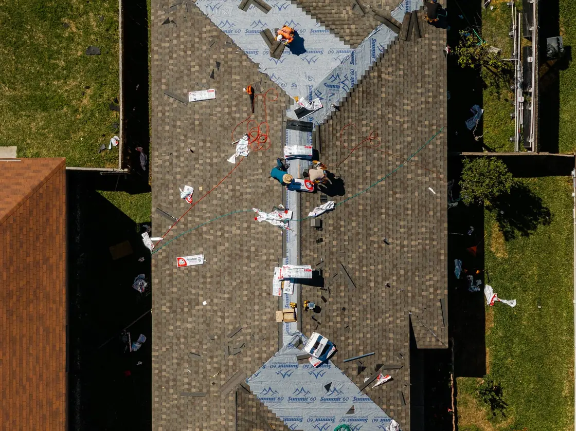 Aerial view of a residential roof mid-installation with decking, underlayment, and shingles going on in layers