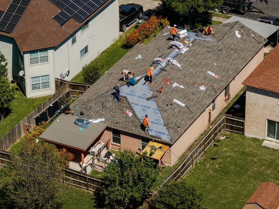 Roofing crew installing asphalt shingles in courses on a Texas home