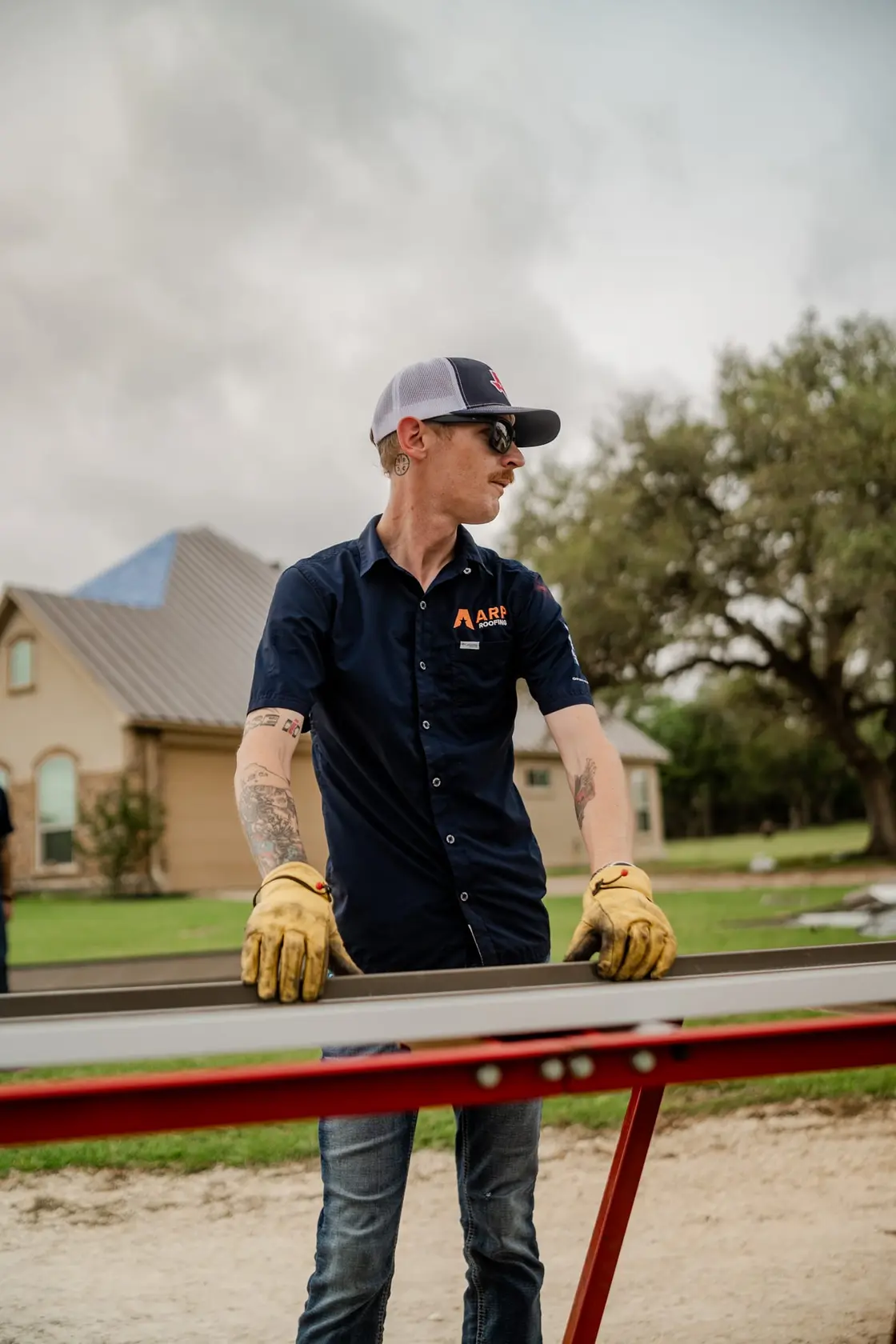 Roofing contractor in a work shirt and gloves handling a metal roofing panel at a residential home