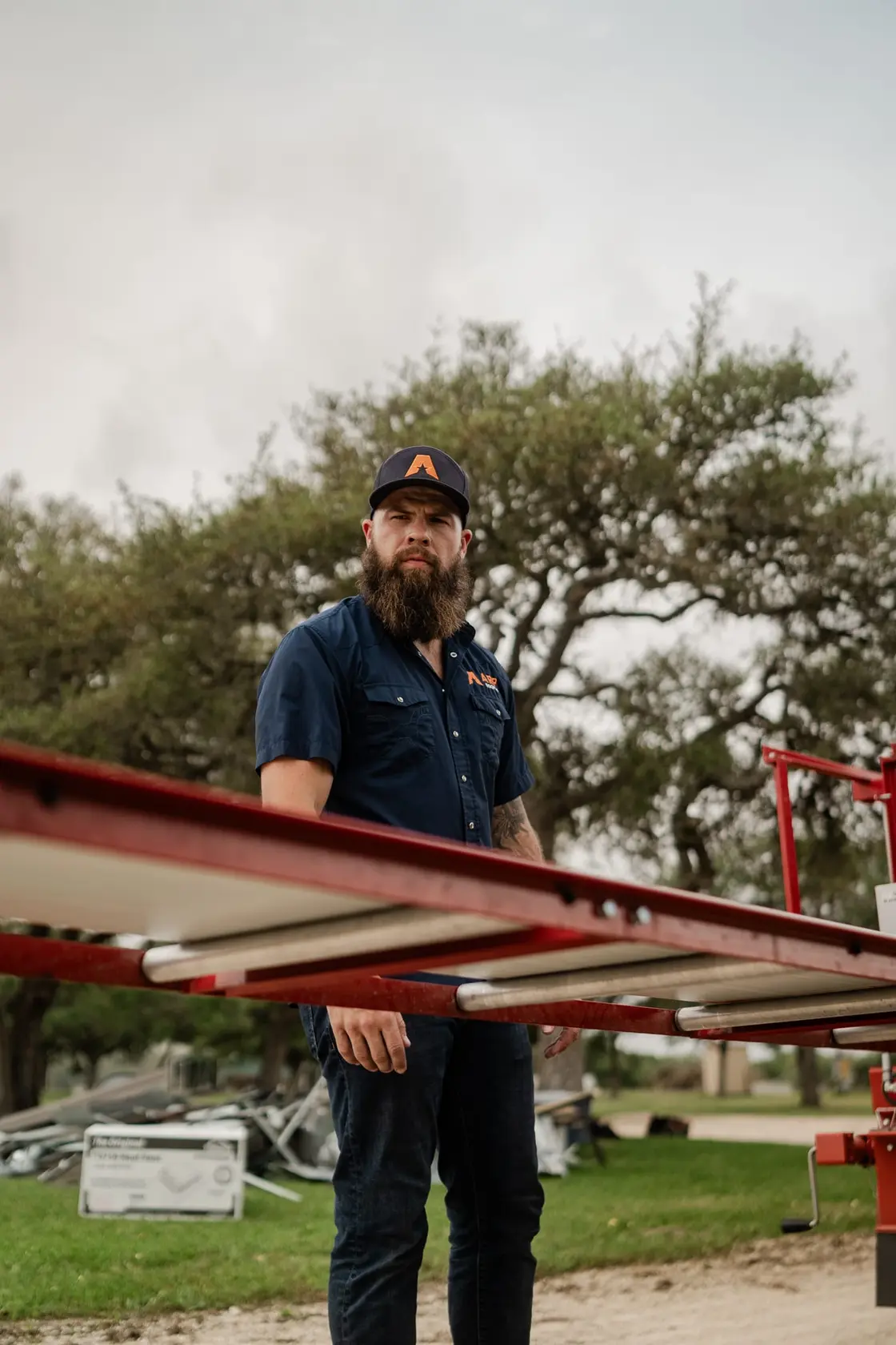 Roofing crew member in a navy work shirt beside metal roof framing at a residential job site