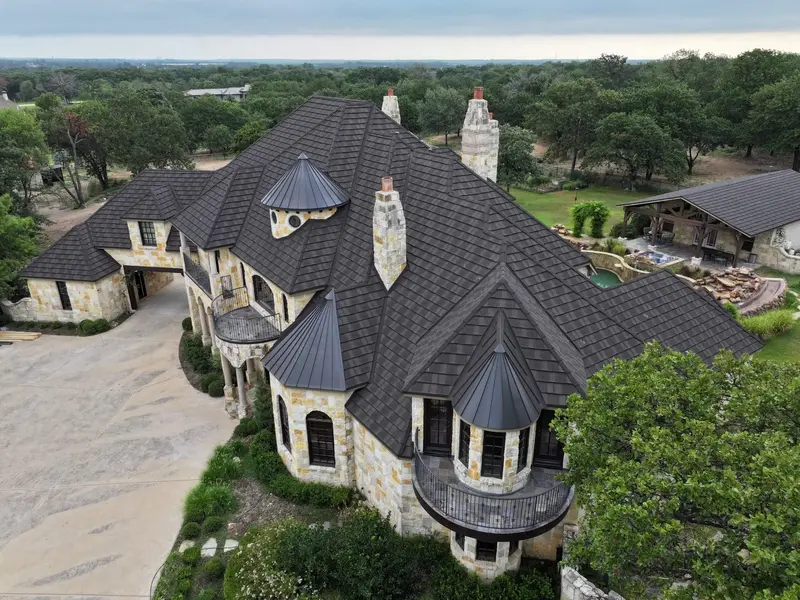 Luxury stone mansion with dark asphalt architectural shingle roof, multiple turrets, metal cupolas, and stone chimneys on