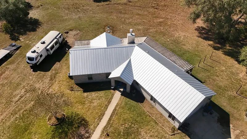 Aerial view of residential home with white metal standing-seam roof and brick exterior, RV parked in driveway